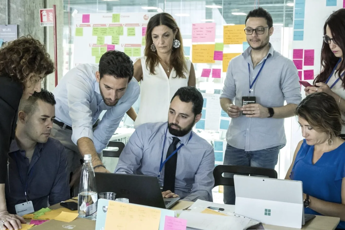 Team al lavoro attorno a un laptop durante un workshop, con muro di post-it alle spalle